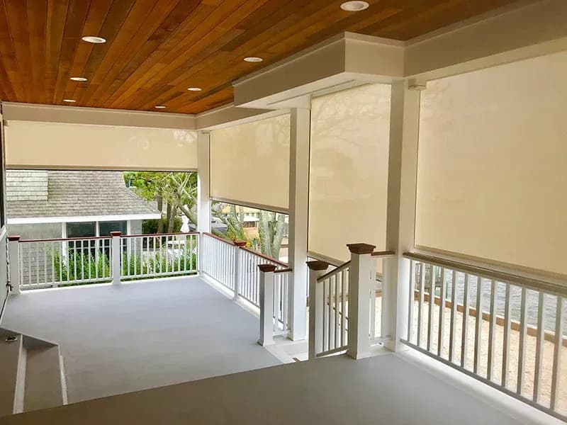 Covered deck with motorized roller shades, white railings, wood ceiling with recessed lights, and view of landscaped yard below